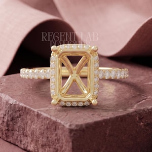 May include: A yellow gold ring setting featuring a rectangular halo of small white diamonds surrounding an empty center. The band is also encrusted with small white diamonds. The text REGENT LAB DIAMONDS is visible above the ring setting.