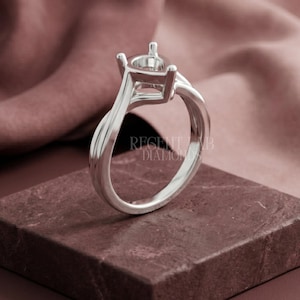 May include: A silver ring setting with a four-prong head, ready for a gemstone. The band features a twisted design. The text "REGENT LAB DIAMONDS" is visible on the ring. The ring is displayed on a maroon surface.