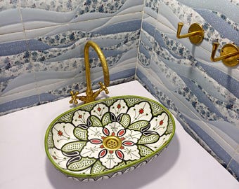 May include: Oval ceramic sink with a floral design in white, green, black, and red. The sink has a gold-colored faucet and is set against a blue and white tiled wall. The sink's dimensions are approximately 20 inches long and 15 inches wide.