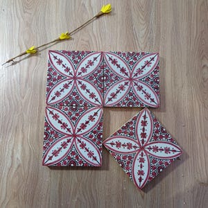 Op de afbeelding: Decoratieve keramische tegels met een bloemmotief in rood en wit. De tegels zijn gerangschikt op een houten oppervlak, met een gele bloemstengel. Geschikt voor interieurontwerp.