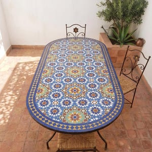 May include: An oval mosaic tile table with a blue, white, and yellow floral pattern. The table is supported by a dark metal frame and is surrounded by two matching chairs with woven seats. A decorative outdoor furniture set.