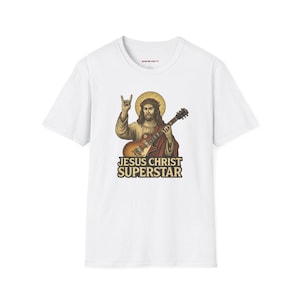 May include: White t-shirt with a graphic of Jesus playing a guitar, wearing a halo and making a rock and roll hand gesture. The text "JESUS CHRIST SUPERSTAR" is below the image in a gold and black font.