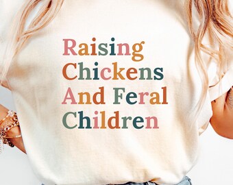 May include: A white t-shirt with the text "Raising Chickens And Feral Children" in colorful letters.