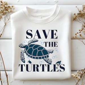 Puede incluir: Sudadera blanca con un gráfico azul de una tortuga marina y el texto "SAVE THE TURTLES".