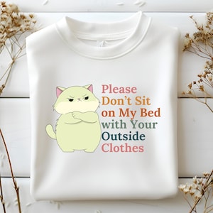 May include: White sweatshirt with a cartoon cat illustration and the text "Please Don't Sit on My Bed with Your Outside Clothes".