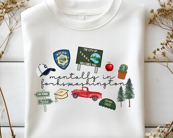 Może przedstawiać: Biała bluza z nadrukiem graficznym. Projekt zawiera napis "mentally in forks washington" oraz ilustracje odznaki policji, znaku, czerwonej ciężarówki, jabłka i innych elementów.