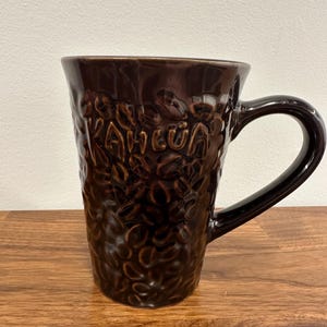 May include: A brown ceramic coffee mug with a textured surface and the word "KAHLUa" embossed on the side. The mug has a large handle.
