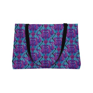 Könnte beinhalten: Eine rechteckige Tragetasche mit einem sich wiederholenden abstrakten Muster in leuchtenden Magenta-, Lila- und Cyan-Blautönen. Die Tasche verfügt über zwei robuste schwarze Stoffgriffe an der Oberkante, die einen Kontrast zum Design bilden.