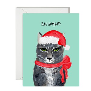 May include: A Christmas greeting card featuring a grumpy gray cat wearing a red Santa hat and scarf with a bow. The words "BAH HUMBUG" are printed above the cat on a teal background. A white envelope is included.