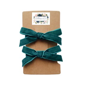 May include: Two teal velvet hair bows on a brown card with a floral logo that says "Doodles and Me Handmade Hair Accessories".