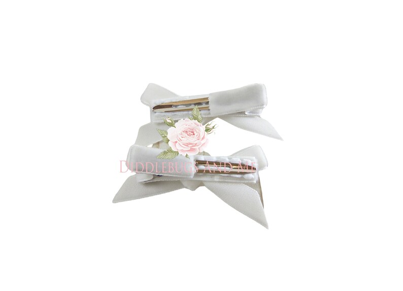 May include: Two white satin hair clips with gold clips. The clips are tied into bows.