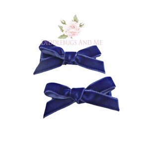 May include: Two navy blue velvet hair bows. The bows are tied in a simple knot and are ready to be clipped into hair.