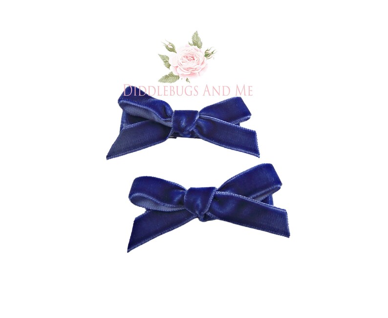 May include: Two navy blue velvet hair bows. The bows are tied in a simple knot and are ready to be clipped into hair.