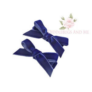 May include: Two navy blue velvet hair bows. The bows are tied in a simple knot and are ready to be worn in hair.