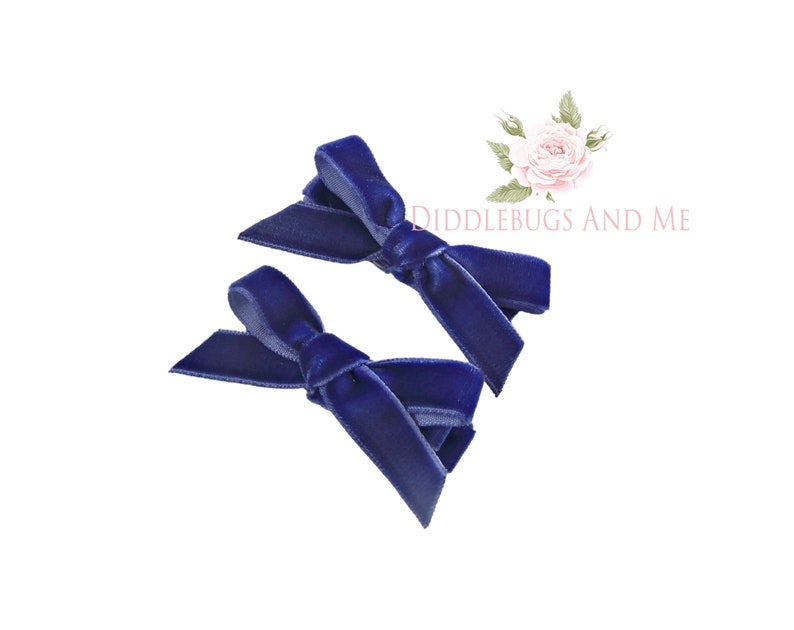 May include: Two navy blue velvet hair bows. The bows are tied in a simple knot and are ready to be worn in hair.