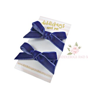 May include: Two navy blue velvet hair bows on a white card with the text "diddlebugs and me" and the website address "www.diddlebugsandme.etsy.com".