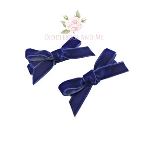 May include: Two navy blue velvet hair bows with a simple knot design.  The bows are attached to alligator clips.