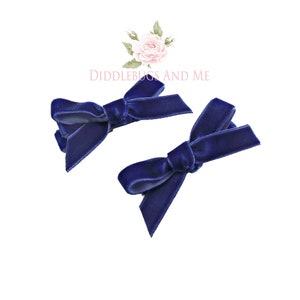 May include: Two navy blue velvet hair bows with a simple knot design.  The bows are attached to alligator clips.