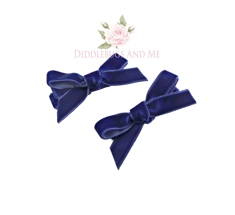 May include: Two navy blue velvet hair bows with a simple knot design.  The bows are attached to alligator clips.