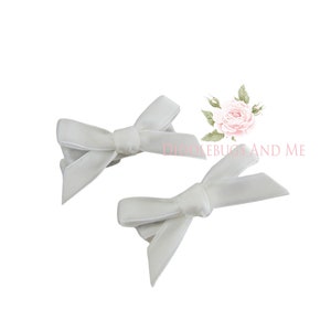 May include: Two white velvet hair bows. The bows are tied in a simple knot and are perfect for adding a touch of elegance to any hairstyle.
