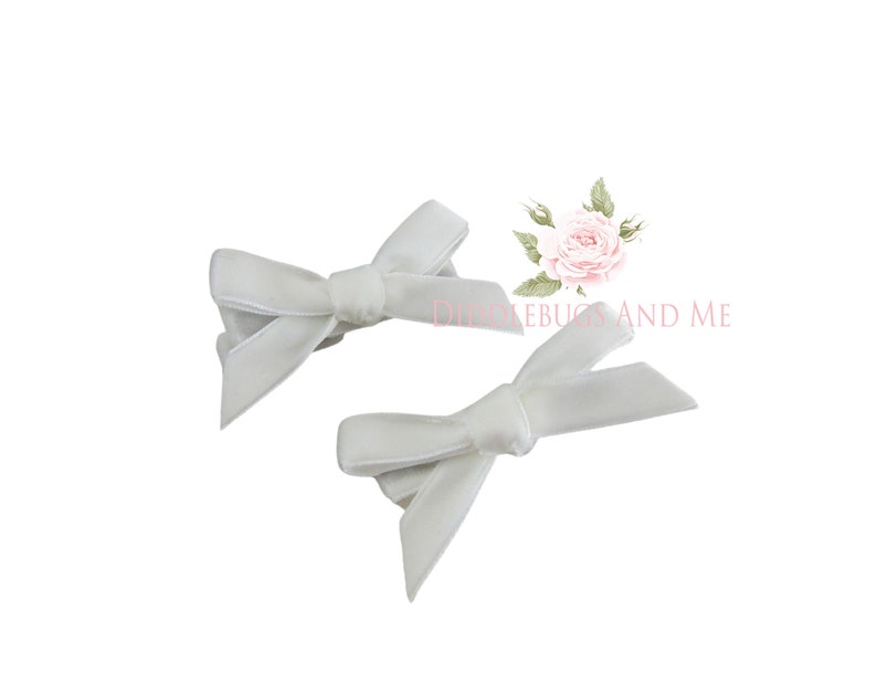 May include: Two white velvet hair bows. The bows are tied in a simple knot and are perfect for adding a touch of elegance to any hairstyle.