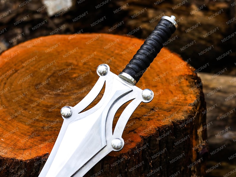May include: A decorative sword with a silver blade and guard, and a black leather-wrapped handle. The sword is displayed on a wooden surface. The guard has four silver studs. The blade is approximately 30 cm long.