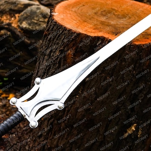 May include: A silver sword with a broad blade and a decorative hilt. The handle is wrapped in black leather. The sword is displayed on a wooden surface. The image includes the text "NSCRAFT".
