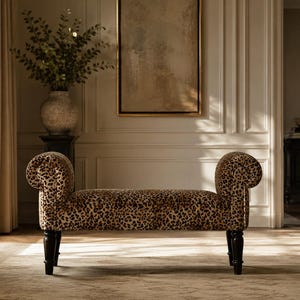 May include: A bench featuring a leopard print fabric upholstery with a rolled armrest on each side. The furniture piece is supported by four dark brown wooden legs that have a tapered design and a smooth, polished finish.