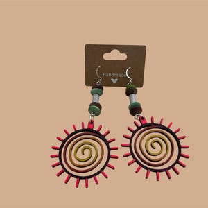 May include: A pair of handmade earrings featuring a red sun with a spiral design and brown, green, and silver beads.