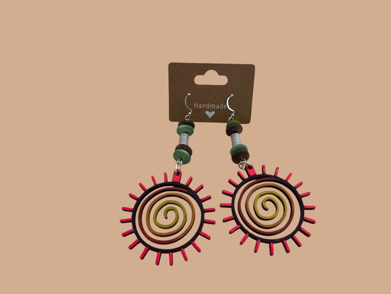 May include: A pair of handmade earrings featuring a red sun with a spiral design and brown, green, and silver beads.