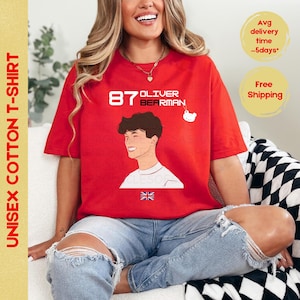 May include: Red cotton t-shirt featuring a cartoon illustration of a young man with the text "87 OLIVER BEARMAN" and a small cartoon bear. The shirt also features a Union Jack flag.