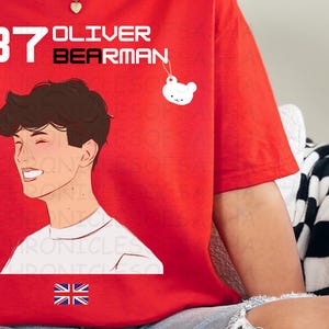 May include: Red t-shirt featuring a white illustration of a person with the text "87 OLIVER BEARMAN" and a small white bear charm.