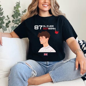 May include: Black t-shirt featuring a white graphic of a racing driver with the text "87 Oliver Bearman" and a small red cherry design.