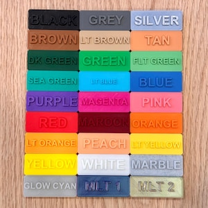 K&ouml;nnte beinhalten: Ein Raster rechteckiger Farbmuster, die jeweils mit einem Farbnamen in erhabenen Buchstaben beschriftet sind. Zu den Farben geh&ouml;ren Schwarz, Grau, Silber, Braun, Beige, Gr&uuml;n, Blau, Lila, Rosa, Rot, Orange, Gelb, Wei&szlig; und Marmor.