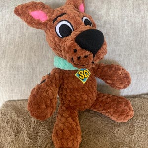 May include: A white ceramic mug with a black handle and the text "But First, Coffee" in a bold, black font. The mug is set against a blurred background, suggesting a cozy setting.