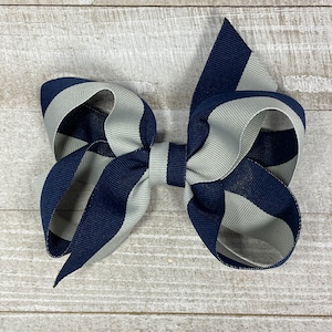 May include: A large navy blue and silver striped hair bow. The bow is made of grosgrain ribbon and is tied in a classic bow shape.