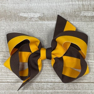 May include: A brown and gold striped hair bow. The bow is made of grosgrain ribbon and is tied in a classic bow shape.