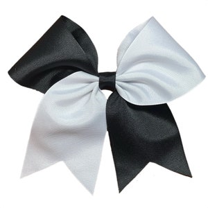 May include: A two-toned hair bow, split vertically with black and white sections. The bow is made of a ribbed fabric and has a classic bow shape with pointed ends. The bow is suitable for cheerleading or other activities.