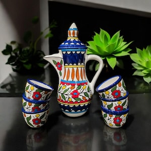 May include: A ceramic coffee set with a decorative coffee pot and six small cups. The set is adorned with a colourful floral design in red, blue, yellow, and green on a white base. The coffee pot has a blue lid and handle, and is suitable for serving coffee.