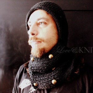 May include: A black knit hat and matching scarf with gold buttons. The hat is pulled down over the person's forehead.