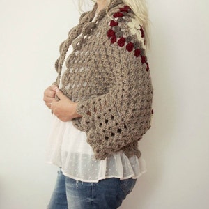 May include: A brown crocheted cardigan with a geometric pattern and red, white, and beige accents. The cardigan has a loose fit and long sleeves.