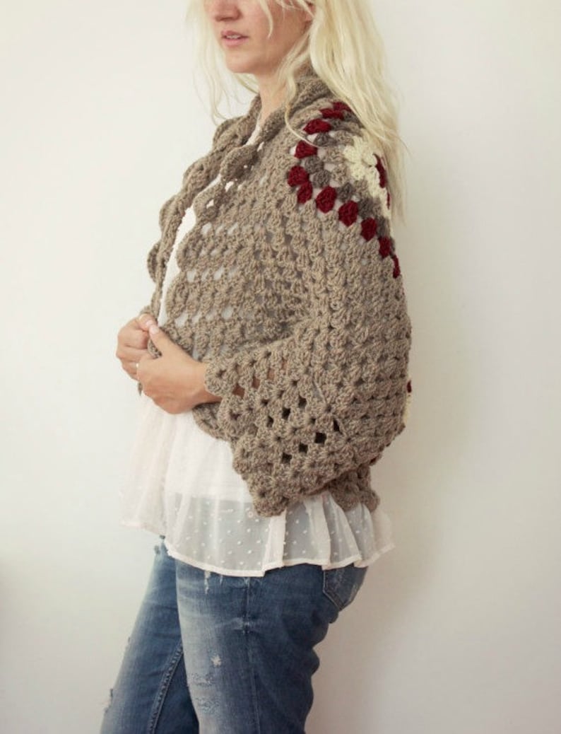 May include: A brown crocheted cardigan with a geometric pattern and red, white, and beige accents. The cardigan has a loose fit and long sleeves.