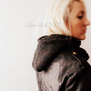 May include: A woman wearing a brown leather jacket with a black knit scarf. The scarf is folded over and covers her neck and ears.