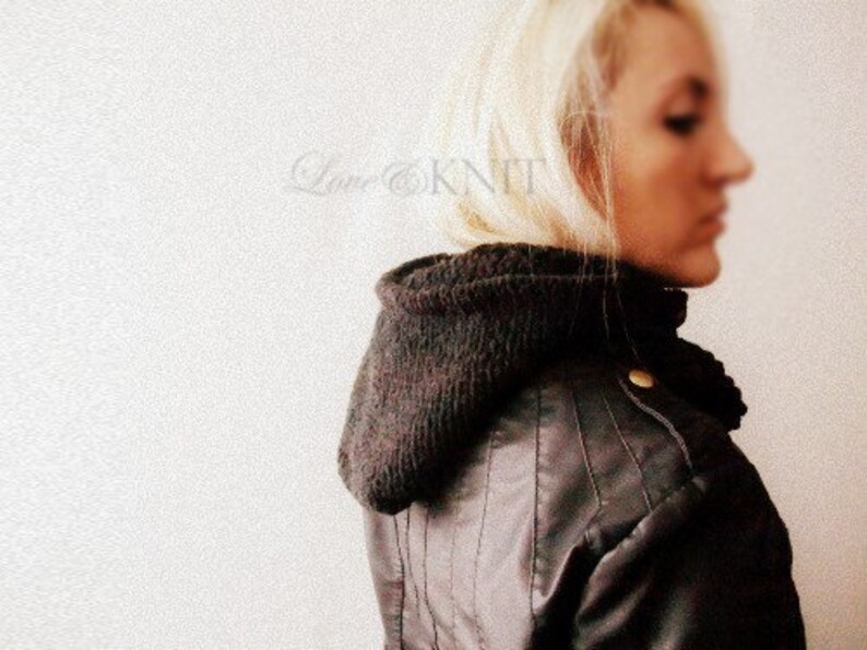 May include: A woman wearing a brown leather jacket with a black knit scarf. The scarf is folded over and covers her neck and ears.