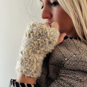 May include: A close-up of a woman's hand wearing a fuzzy, light brown and gold fingerless glove. The glove has a sparkly texture and is made of a soft, warm material.