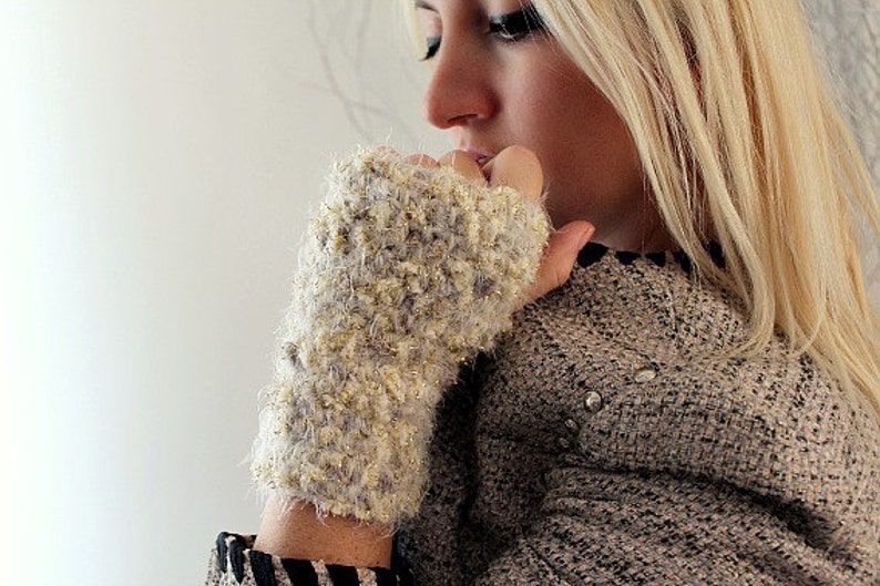 May include: A close-up of a woman's hand wearing a fuzzy, light brown and gold fingerless glove. The glove has a sparkly texture and is made of a soft, warm material.