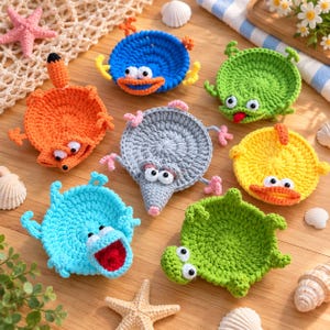 May include: A collection of seven round, crocheted coasters shaped like various animals, including a blue fish, a green frog, an orange fox, a gray mouse, a yellow duck, a light blue creature, and a green turtle, all featuring googly eyes.