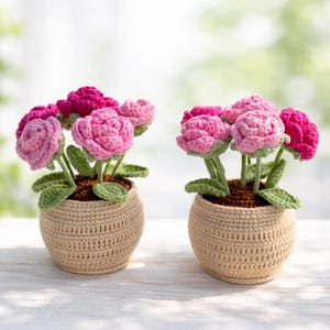 May include: Two crochet flower pots, each filled with pink and fuchsia flowers and green leaves. The flowers are in beige crochet pots. The background is a soft, blurred green.