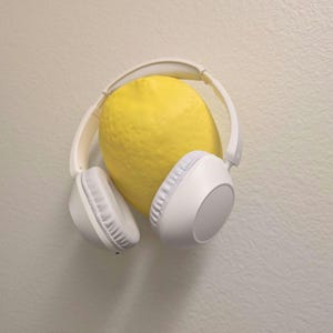 May include: A bright yellow lemon nestled inside a pair of white over-ear headphones. The headphones have a padded headband and earcups. The background is a neutral, off-white color.