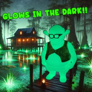 May include: A green, glowing figure of Shrek standing on a wooden dock in a swamp. The swamp is filled with glowing green water and plants. The text "GLOWS IN THE DARK!" is written in green letters at the top of the image.